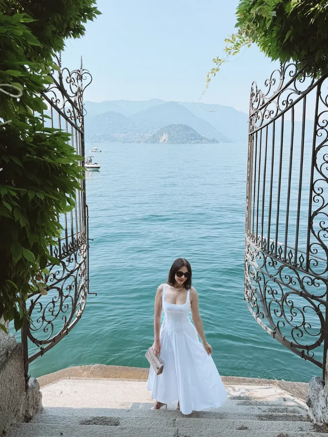 A white gown at an ornate iron gate overlooking a lake