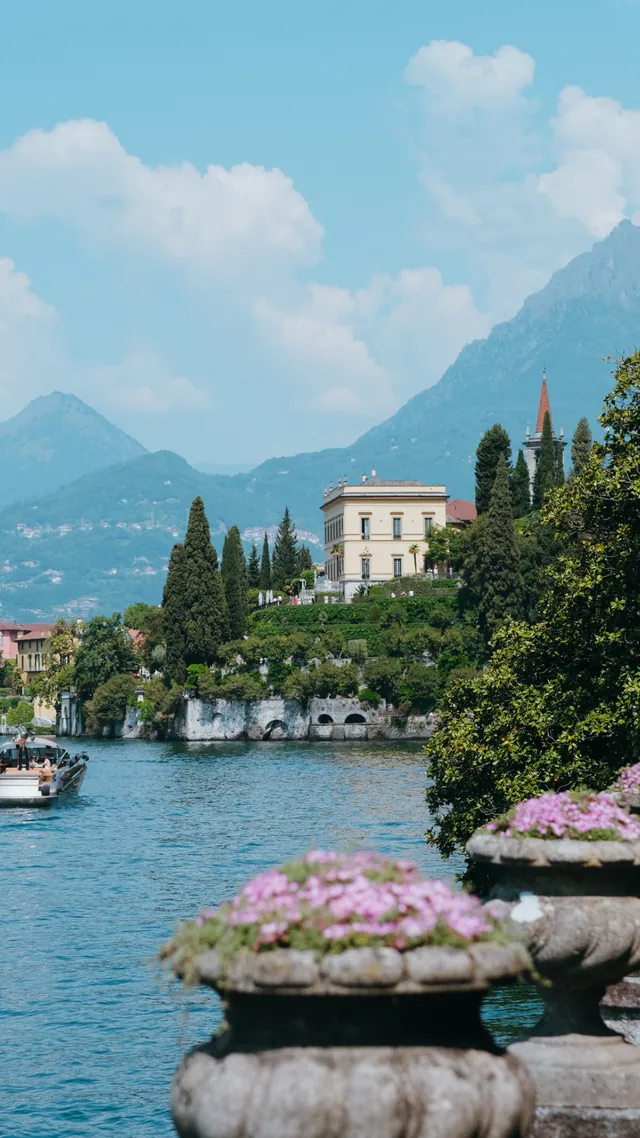 A historic villa above a lake with pink flowers in stone urns